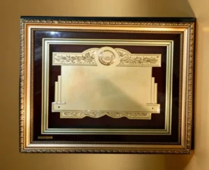 Plaqueta conmemorativa tipo cuadro con acabado en oro, marco decorativo y estuche de lujo de Nevey Medallas. Modelo 1900