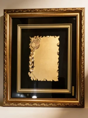 Plaqueta conmemorativa tipo cuadro con acabado en oro, marco decorativo y estuche de lujo de Nevey Medallas. Modelo 2100
